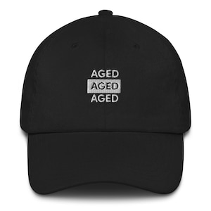 May include: Black baseball cap with white embroidered text that reads "AGED AGED AGED".