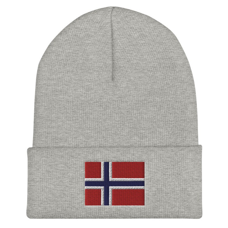 May include: A gray beanie featuring the flag of Norway embroidered on the front. The flag design includes a red background with a blue cross outlined in white. The beanie is a simple, casual style.