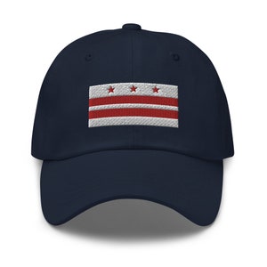 May include: A navy blue baseball cap with an embroidered patch of the District of Columbia flag. The flag features three red stars and three red stripes on a white background.