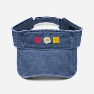 May include: A blue denim visor with a red circle, a white egg, and a yellow square embroidered on the front.