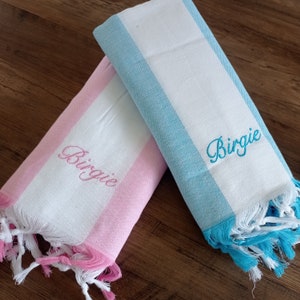 May include: Two striped towels with fringe edges. One towel is pink and white with the name Birgie embroidered in pink. The other towel is blue and white with the name Birgie embroidered in blue.