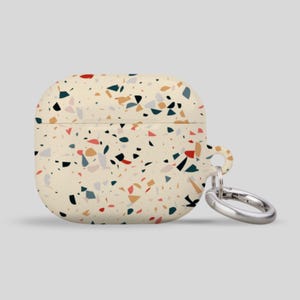 May include: A white Airpods case with a terrazzo pattern in shades of red, blue, and yellow. The case has a silver metal keychain attached.