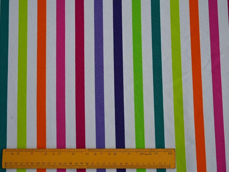 May include: A fabric with vertical stripes in various colors, including green, orange, pink, purple, and teal, against a white background. A yellow ruler is at the bottom of the image, measuring the fabric.