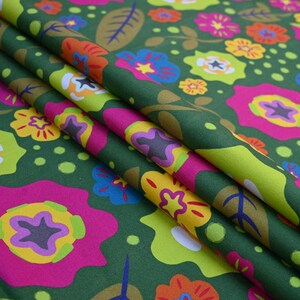 May include: Green fabric with a vibrant floral pattern. The design features large, stylized flowers in shades of pink, yellow, blue, and orange, set against a dark green background. The fabric is folded, showing the pattern's repeat.