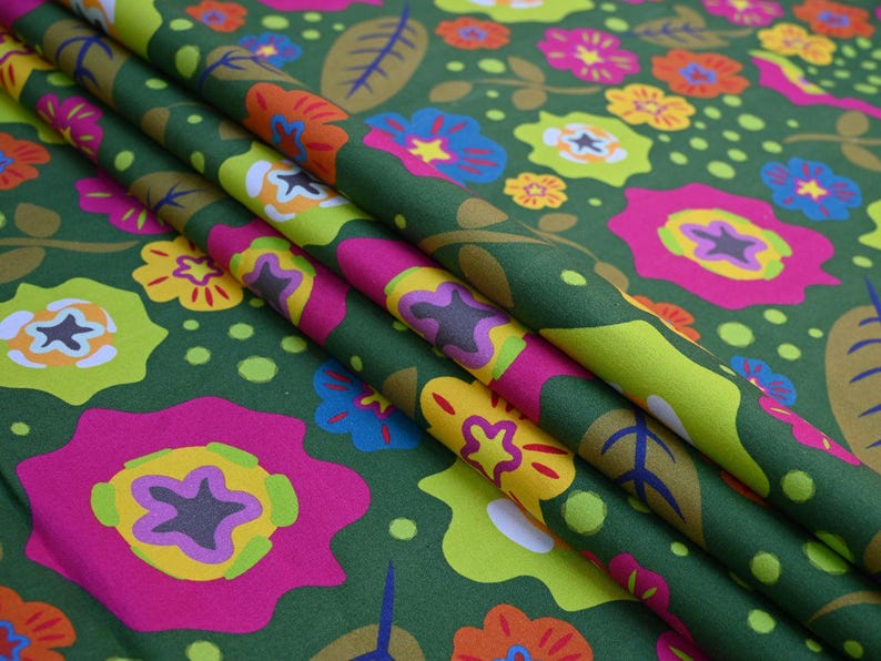 May include: Green fabric with a vibrant floral pattern. The design features large, stylized flowers in shades of pink, yellow, blue, and orange, set against a dark green background. The fabric is folded, showing the pattern's repeat.