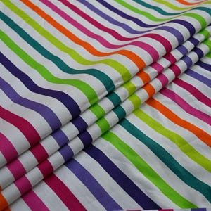 May include: A folded fabric with a white background and vibrant, colorful stripes in shades of pink, orange, green, purple, and teal. The stripes run diagonally across the fabric, creating a playful and eye-catching pattern. This textile is suitable for various craft projects.