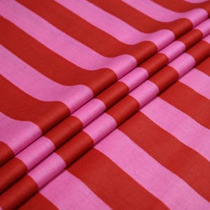 May include: Close-up of a fabric with bold, alternating stripes in shades of red and pink. The fabric is folded, creating a textured effect. The stripes run diagonally across the image, adding visual interest. This textile is suitable for various sewing projects.
