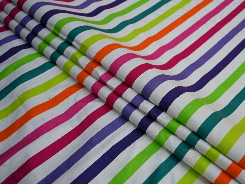 May include: Fabric with a repeating pattern of colorful, wavy stripes in shades of purple, pink, orange, green, and blue on a white background. The fabric is folded, showing the texture and layers of the material.