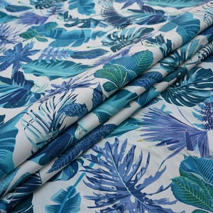 May include: White fabric with a vibrant tropical leaf pattern in shades of blue and teal. The design features large, detailed leaves and smaller, more delicate foliage, creating a lush, botanical theme.