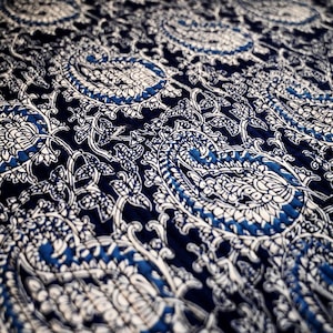 Puede incluir: Primer plano de una tela con estampado azul y blanco con diseño paisley. La tela está acolchada y tiene un tacto suave y texturizado.
