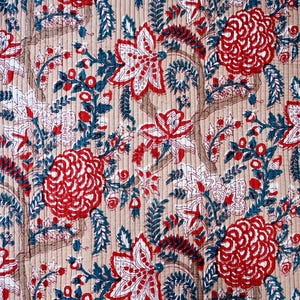 May include: Close-up of a floral pattern textile. The design features large red and white flowers, teal leaves, and brown stems on a beige background. The fabric has a quilted texture.