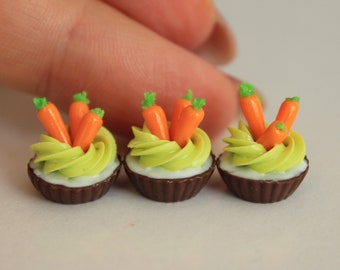 Peut inclure: Mini-cupcakes avec des bases couleur chocolat, surmontés d'un glaçage vert clair et de décorations de carottes orange. Les cupcakes sont disposés en rangée, présentant un design fantaisiste sur le thème de la nourriture.