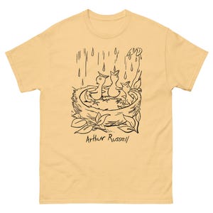 May include: A yellow t-shirt with a black line drawing of three birds in a nest with rain falling. The text "Arthur Russell" is below the drawing.