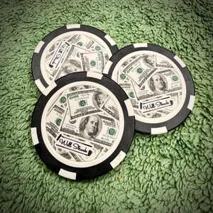Puede incluir: Tres fichas de p&oacute;quer en blanco y negro con un dise&ntilde;o de billetes de 100 $. Las fichas tienen el texto "Will Struck". Est&aacute;n sobre una superficie verde texturizada.