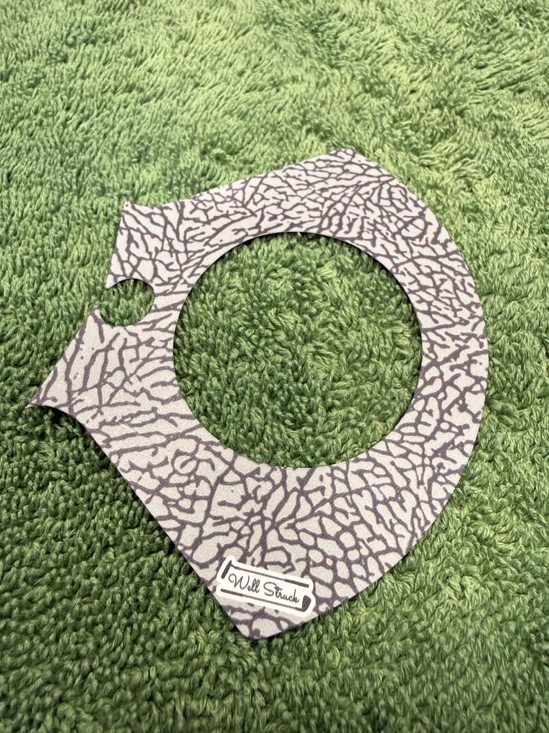 Pu&ograve; includere: Un accessorio grigio e bianco a fantasia con un ritaglio circolare. Il motivo ricorda la pelle di elefante. Il testo "Will Struck" &egrave; stampato su una piccola etichetta bianca nella parte inferiore dell'accessorio.