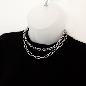 May include: A silver chain necklace featuring two different chain styles. The necklace is layered with a thicker, round chain and a thinner, rectangular chain.