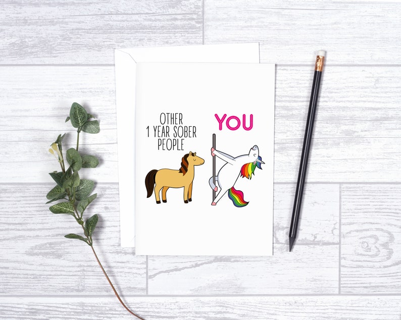 Pu&ograve; includere: Un biglietto d'auguri bianco con un cavallo color marrone chiaro in stile cartoon accanto al testo OTHER 1 YEAR SOBER PEOPLE e un unicorno con criniera arcobaleno che danza su un palo accanto al testo rosa YOU, con busta bianca.