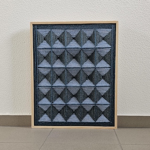 May include: A rectangular wall art piece featuring a grid of sixteen pyramid-shaped structures created with dark blue and black yarn. The yarn is wrapped tightly to form geometric patterns within a light-colored wooden frame, creating a textured effect.