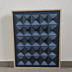 May include: A square wall art piece featuring a light wood frame and a dark blue string art design. The artwork consists of a grid of sixteen pyramid-like shapes created by tightly wound blue thread, forming a repeating geometric pattern.