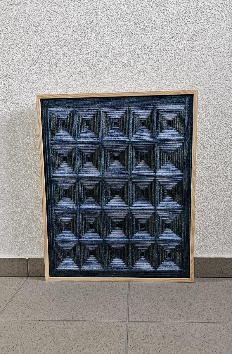 May include: A square wall art piece featuring a light wood frame and a dark blue string art design. The artwork consists of a grid of sixteen pyramid-like shapes created by tightly wound blue thread, forming a repeating geometric pattern.