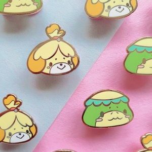 Op de afbeelding: Een set emaillepins met personages uit de Animal Crossing-videogameserie. De pins zijn kleurrijk en bevatten verschillende personages, waaronder Isabelle, een hond en een kikker. De pins zijn perfect om een vleugje whimsy toe te voegen aan je rugzak, jas of andere accessoires.