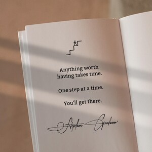 May include: An open book page featuring a black line drawing of a person climbing stairs. The text reads: Anything worth having takes time. One step at a time. You'll get there. Below the text is the signature of Stephen Graham in black ink.
