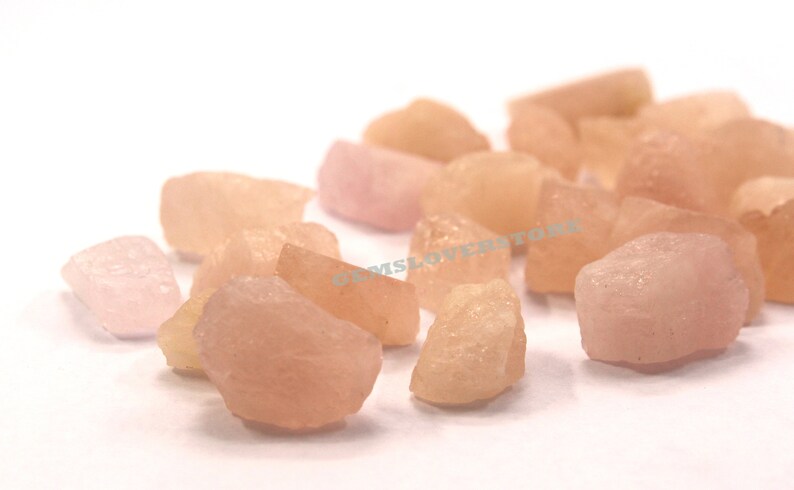 Pode incluir: Uma cole&ccedil;&atilde;o de gemas brutas rosa e laranja. As pedras s&atilde;o de v&aacute;rios tamanhos e formas, algumas tendo uma apar&ecirc;ncia mais transl&uacute;cida do que outras.