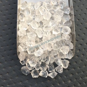 Pode incluir: Uma visão de perto de um monte de cristais de quartzo transparentes. Os cristais são de vários tamanhos e formas, e todos são muito brilhantes.