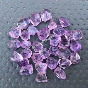May include: A collection of raw amethyst crystals in various sizes and shapes. The crystals are a light purple colour and have a natural, rough texture.