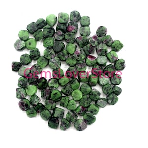 Könnte beinhalten: Eine Sammlung grüner und roter Edelsteinchipse, wahrscheinlich Zoisit, in facettierter Form. Die Chips sind auf einem weißen Hintergrund verstreut.
