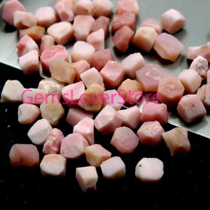 May include: A pile of small, pink, rough-cut opal gemstones. The stones are various shades of pink and have a slightly iridescent sheen.