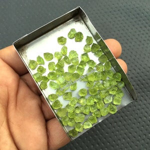 May include: A small metal tray filled with a large quantity of rough, green peridot gemstones.