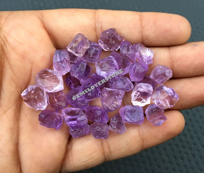 May include: A pile of small, rough, purple amethyst crystals. The crystals are translucent and have a variety of shapes and sizes.