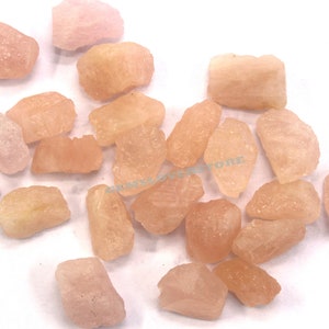 Pode incluir: Uma cole&ccedil;&atilde;o de pedras preciosas brutas rosa e laranja. As pedras s&atilde;o de v&aacute;rios formatos e tamanhos, e t&ecirc;m um acabamento natural n&atilde;o polido.