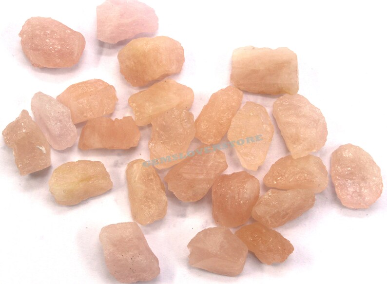 Pode incluir: Uma cole&ccedil;&atilde;o de pedras preciosas brutas rosa e laranja. As pedras s&atilde;o de v&aacute;rios formatos e tamanhos, e t&ecirc;m um acabamento natural n&atilde;o polido.