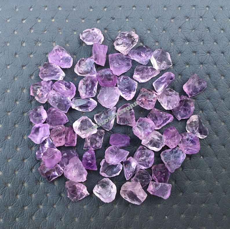 May include: A collection of approximately 50 small, rough-cut amethyst crystals. The crystals are a light purple color and have a variety of shapes and sizes.