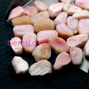 May include: A collection of pink opal rough stones. The stones are various sizes and shapes, and have a natural, unpolished finish.
