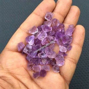 May include: A small pile of purple amethyst crystals in a hand. The crystals are rough and have a natural, unpolished look.