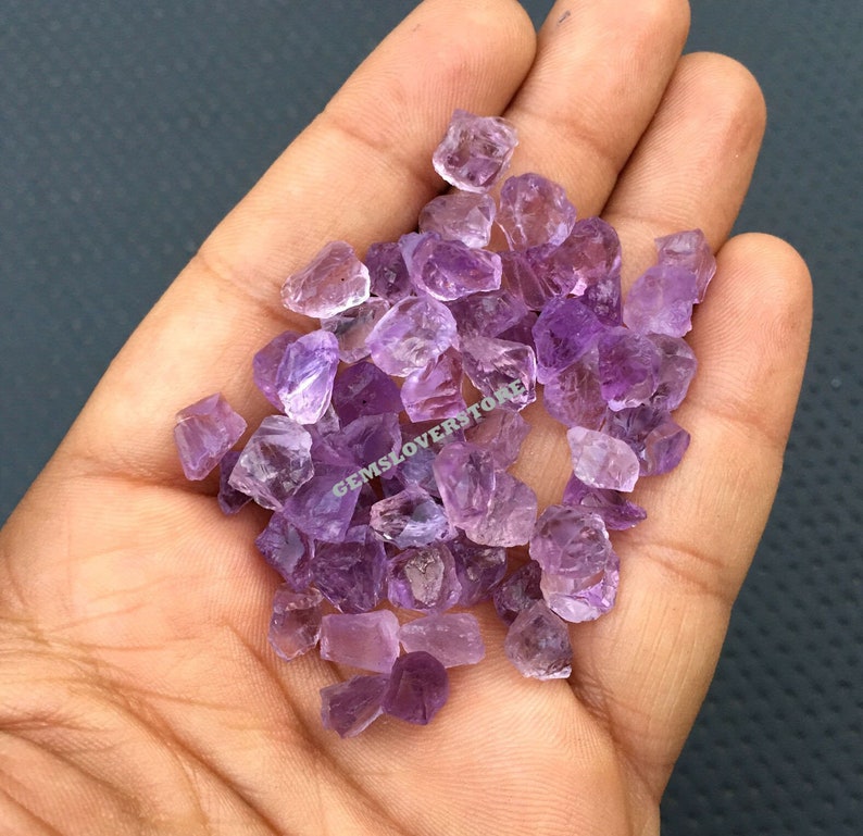 May include: A small pile of purple amethyst crystals in a hand. The crystals are rough and have a natural, unpolished look.