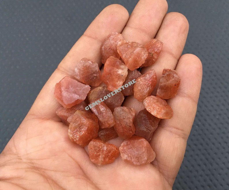 K&ouml;nnte beinhalten: Ein Haufen kleiner, rauer, orange-roter Sunstone-Kristalle. Die Kristalle sind durchscheinend und haben einen leichten Glanz.