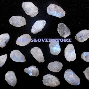 May include: A collection of 20 raw, white moonstone crystals with iridescent blue and green flashes. The crystals are various sizes and shapes, with some being more pointed than others.