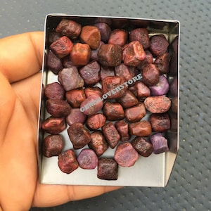 Peut inclure: Une collection de petites pierres précieuses brutes, rouges et violettes, dans un plateau en métal. Les pierres précieuses sont probablement des rubis.