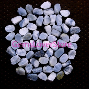 May include: A collection of approximately 40 light blue and white opal gemstone chips. The chips are irregularly shaped and have a smooth, polished finish.  GemsloverStore is printed in pink on the image.