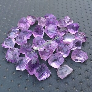 May include: A pile of raw amethyst crystals in various sizes and shapes. The crystals are a light purple colour and have a natural, rough texture.