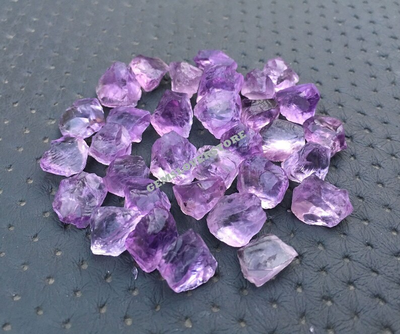 May include: A pile of raw amethyst crystals in various sizes and shapes. The crystals are a light purple colour and have a natural, rough texture.