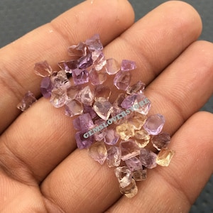 May include: A pile of small, faceted amethyst and citrine gemstones in various shades of purple and yellow. The gemstones are loose and scattered on a hand.