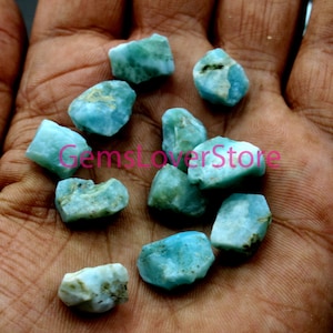 Puede incluir: Una colección de chips de piedras preciosas crudas, de color azul claro y verde. Los chips son de forma irregular y tienen una apariencia translúcida.