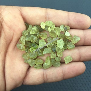 Pode incluir: Um monte de pequenas pedras preciosas verdes brutas. As pedras preciosas são translúcidas e têm um tom ligeiramente amarelo.