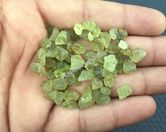 May include: A pile of small, rough, green gemstones. The gemstones are translucent and have a slightly yellow hue.