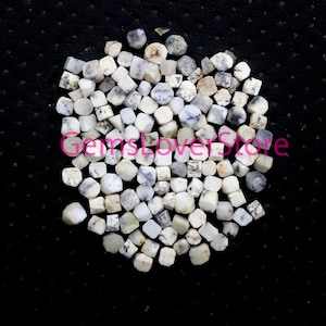 May include: A pile of white and gray gemstone beads, each bead is a cube with rounded edges. The beads are on a black background.